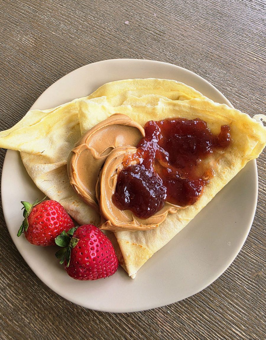 The kids pb&j crêpe on a pale plate — a folded crêpe spread with peanut butter and strawberry jam, with two whole strawberries alongside