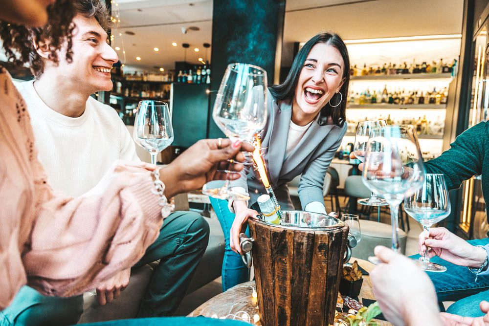 Friends laughing and raising glasses around a table with a sparkler in a champagne bucket