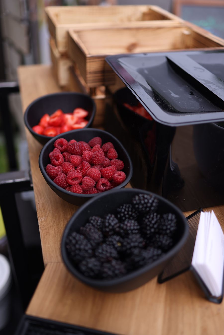Bowls of sliced strawberries, raspberries and blackberries lined up on the wooden serving counter of the crêpe stand
