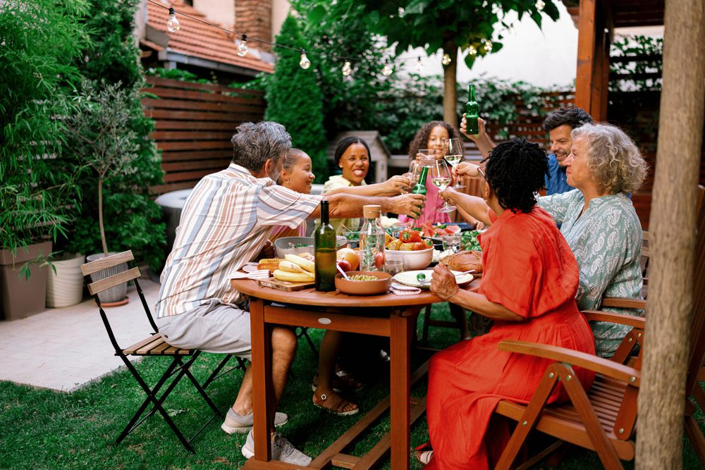 A family of all ages toasting around a laden table in a leafy back garden strung with lights